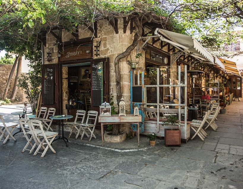 Casa Cook Rhodes Greece outside of a local cafe with tresell chairs outside the cafe in the square