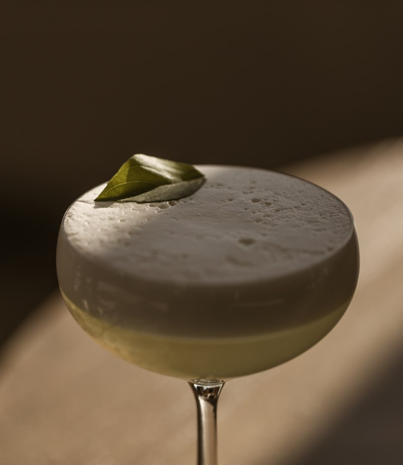 Cocktail with foam and herb garnish sitting on a table at Casa Cook Rhodes Bar