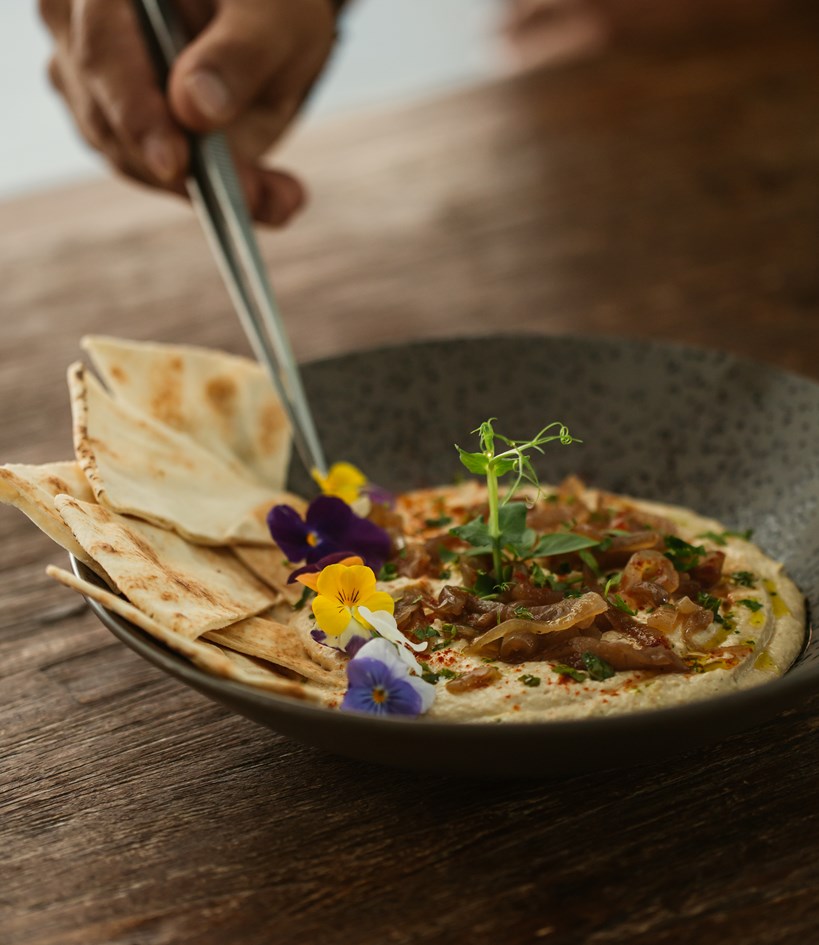 Chef garnishing a plate of freshly made hummus with toasted pita bread